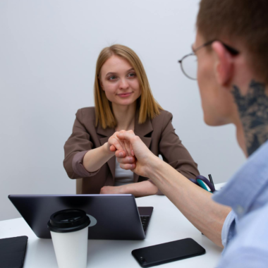Two business professionals shaking hands across a desk, symbolizing teamwork and collaboration.